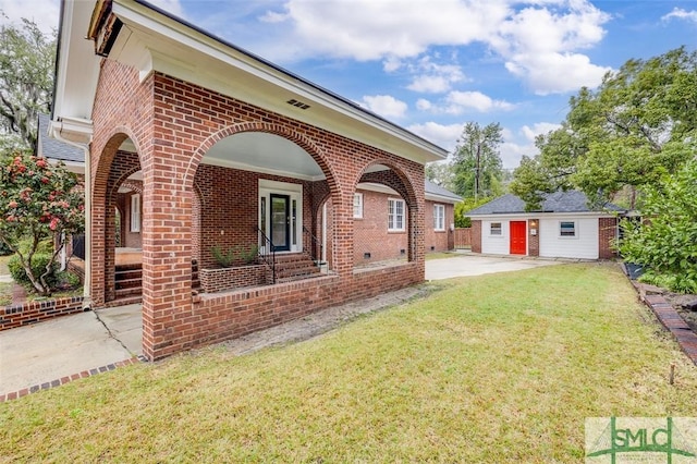 exterior space featuring an outbuilding, covered porch, a lawn, and brick siding