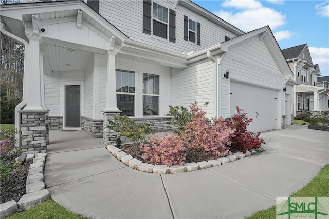 view of property exterior with driveway, stone siding, board and batten siding, covered porch, and a garage