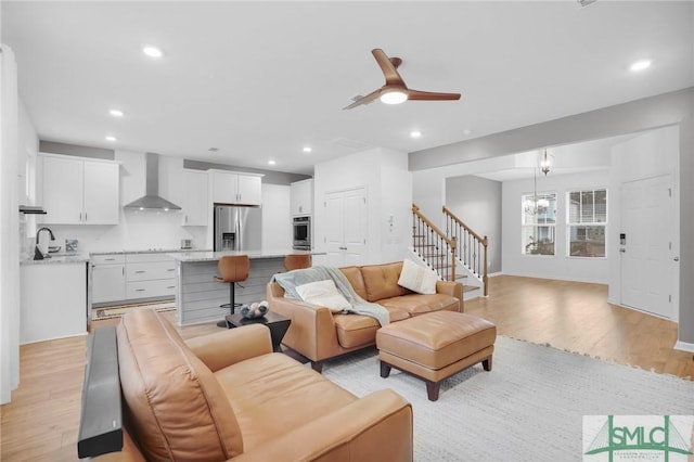 living area with recessed lighting, ceiling fan with notable chandelier, stairs, and light wood finished floors