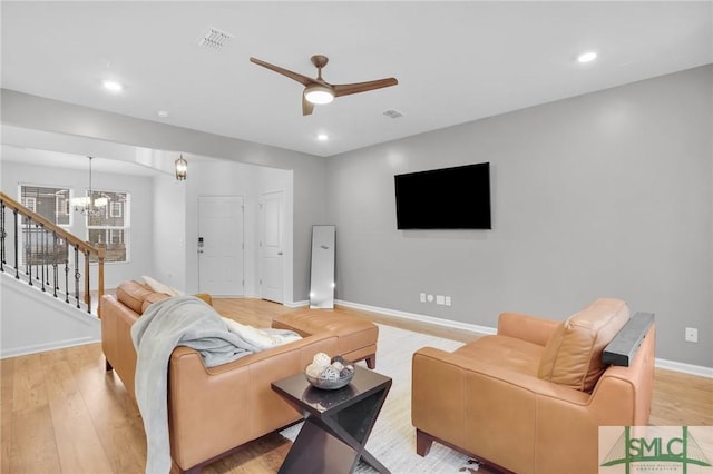 living room featuring visible vents, baseboards, light wood-style flooring, and ceiling fan with notable chandelier