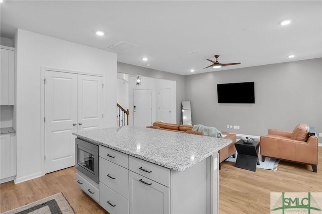 kitchen with light wood finished floors, stainless steel microwave, a kitchen island, open floor plan, and recessed lighting