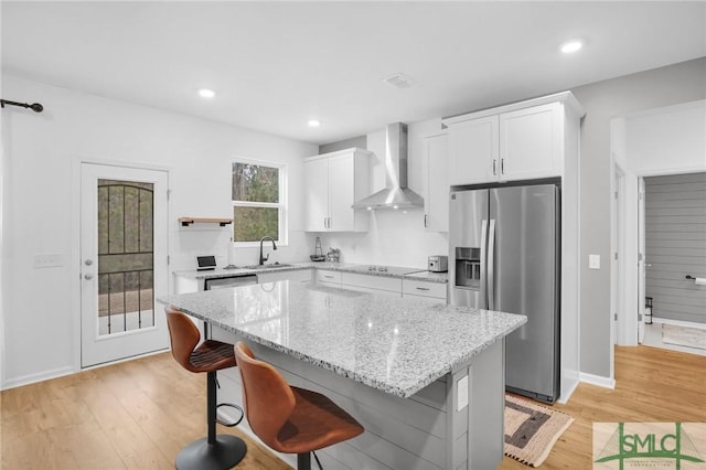 kitchen with light wood finished floors, a sink, stainless steel refrigerator with ice dispenser, wall chimney range hood, and a center island