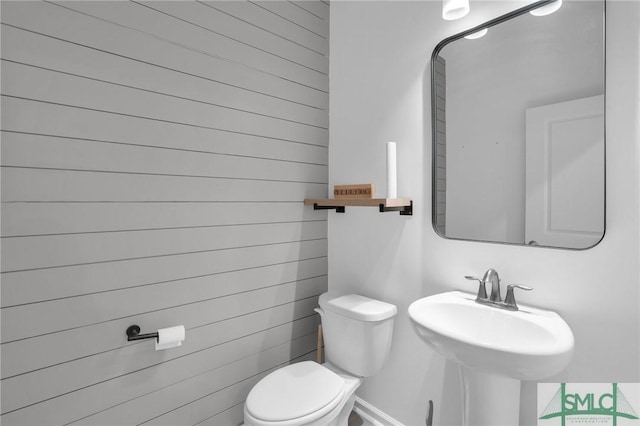 bathroom featuring a sink, toilet, and wooden walls