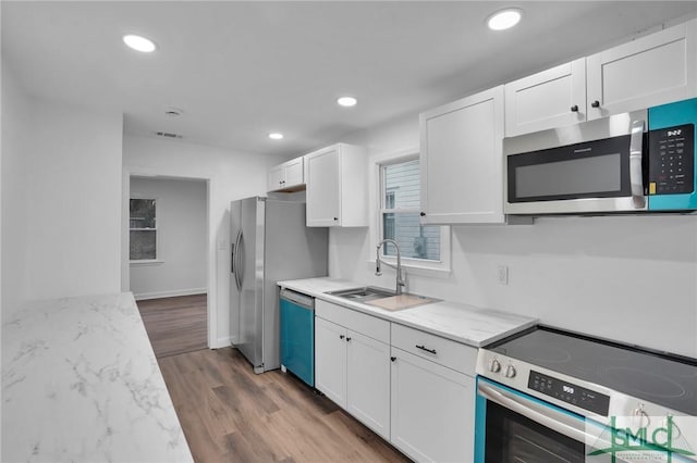 kitchen with recessed lighting, wood finished floors, white cabinets, stainless steel appliances, and a sink