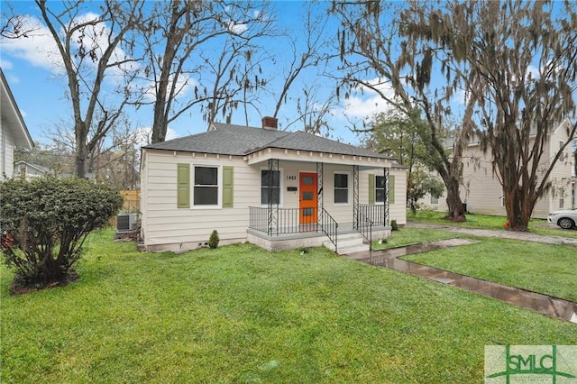 bungalow featuring central air condition unit, a chimney, a front yard, and a shingled roof