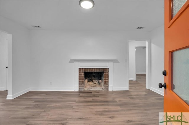 unfurnished living room with wood finished floors, a fireplace, visible vents, and baseboards