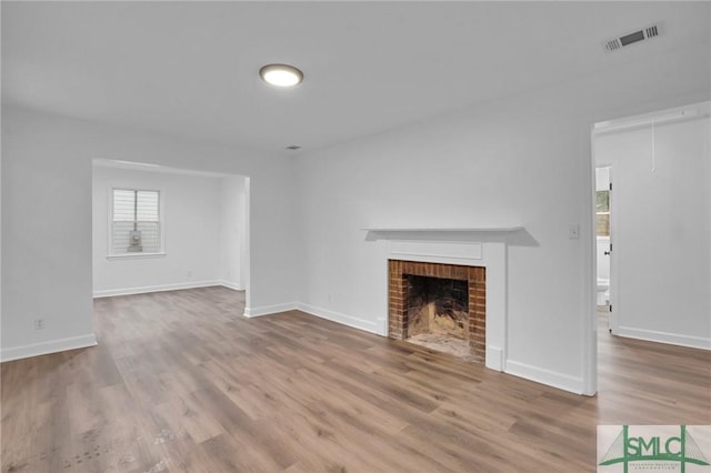 unfurnished living room featuring a fireplace, attic access, wood finished floors, and visible vents