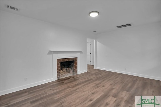 unfurnished living room featuring a brick fireplace, wood finished floors, and visible vents