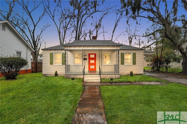 bungalow-style home featuring covered porch, a chimney, a front yard, and fence