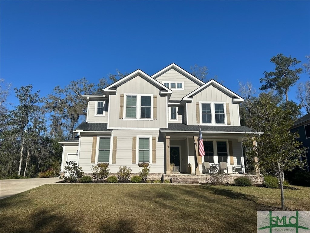 view of front facade with board and batten siding, covered porch, concrete driveway, and a front lawn