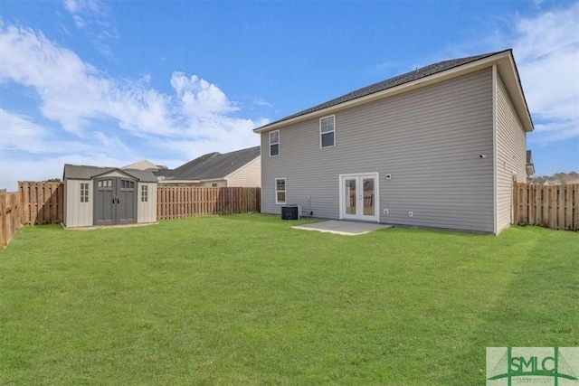 rear view of property featuring a lawn, french doors, a storage shed, a fenced backyard, and an outbuilding