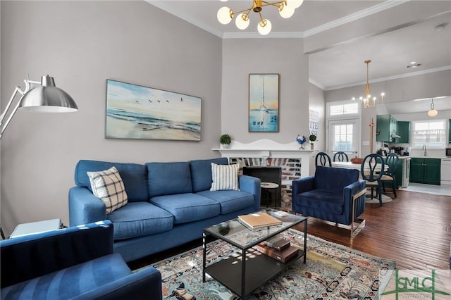 living room with crown molding, a brick fireplace, a notable chandelier, and wood finished floors