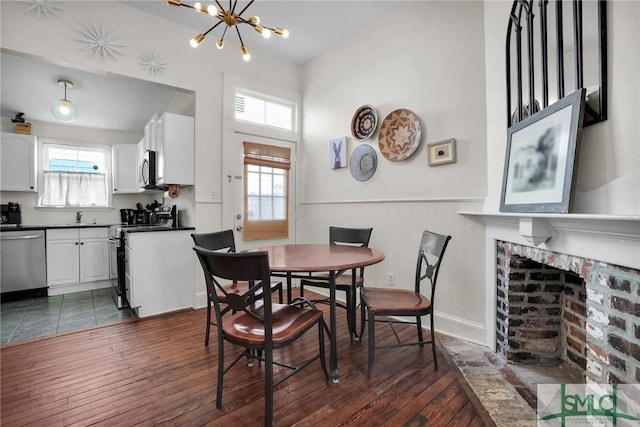 dining room featuring a fireplace, a notable chandelier, dark wood-style floors, and a wainscoted wall