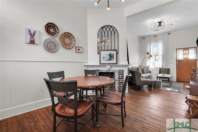 dining room featuring an inviting chandelier, a fireplace, wood-type flooring, and wainscoting