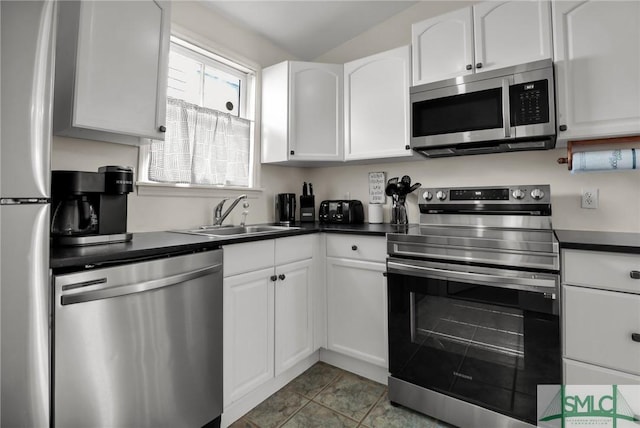 kitchen featuring dark countertops, tile patterned flooring, appliances with stainless steel finishes, white cabinetry, and a sink