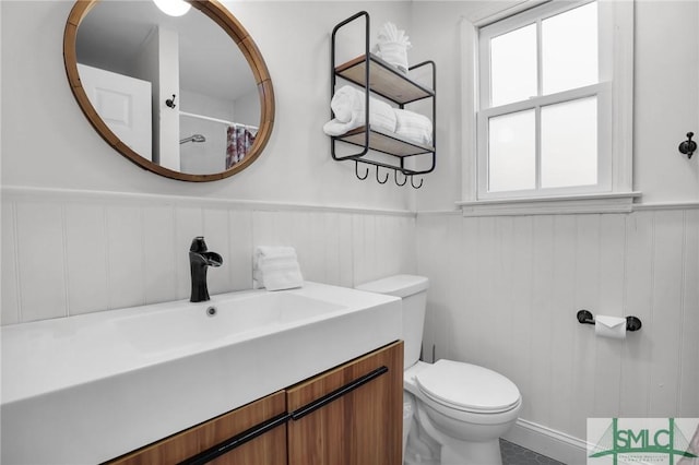 bathroom featuring a shower with curtain, vanity, toilet, and wainscoting