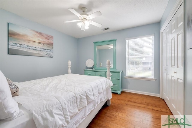 bedroom with visible vents, a ceiling fan, wood finished floors, a closet, and baseboards