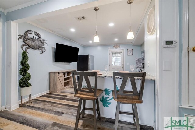 kitchen with visible vents, ornamental molding, light stone counters, freestanding refrigerator, and wood finished floors