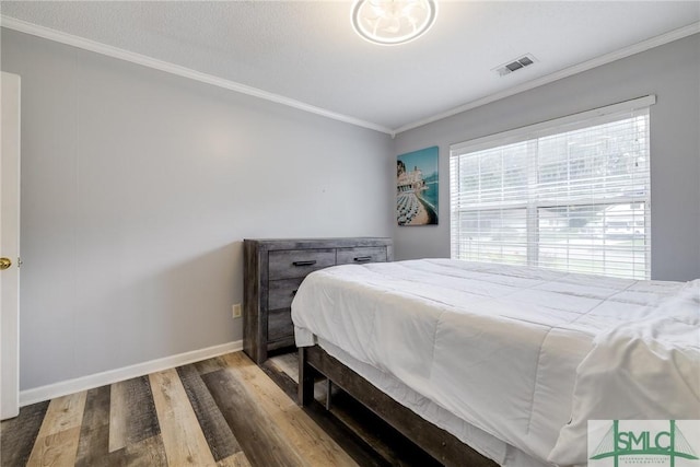 bedroom with visible vents, crown molding, baseboards, and wood finished floors