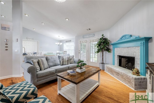 living room with visible vents, a fireplace, light wood finished floors, a chandelier, and vaulted ceiling