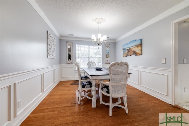 dining room with a notable chandelier, light wood-style flooring, a textured ceiling, and ornamental molding