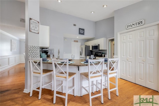 kitchen with white cabinetry, stainless steel appliances, a peninsula, wainscoting, and light wood finished floors