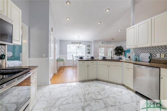 kitchen featuring a wainscoted wall, marble finish floor, a sink, stainless steel appliances, and a peninsula