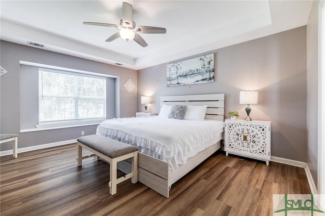 bedroom featuring a tray ceiling, visible vents, baseboards, and wood finished floors