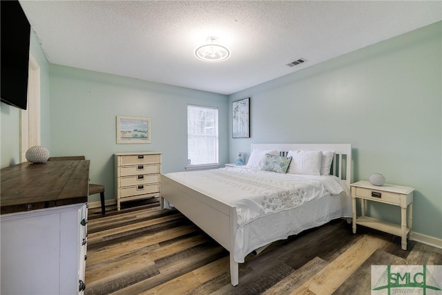 bedroom featuring dark wood finished floors, baseboards, visible vents, and a textured ceiling