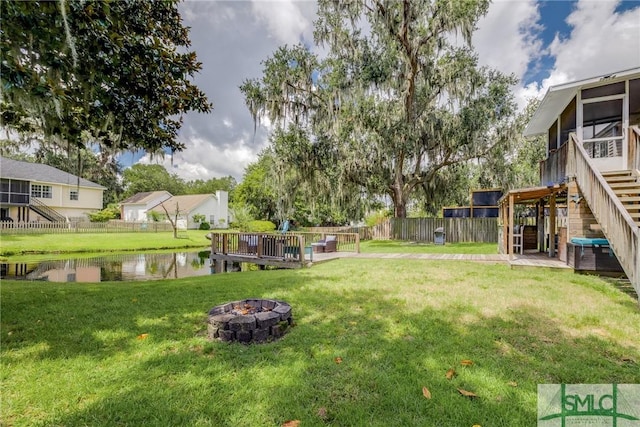 view of yard with a fire pit, fence, stairs, a sunroom, and a deck with water view