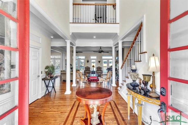 foyer entrance featuring ornamental molding, decorative columns, stairs, light wood-style floors, and a ceiling fan