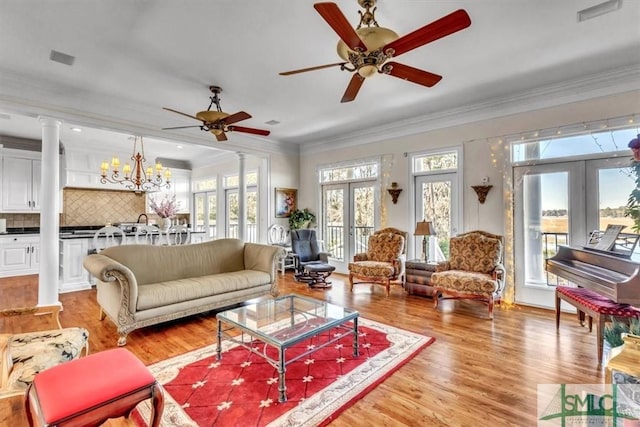 living room featuring crown molding, decorative columns, light wood finished floors, and ceiling fan with notable chandelier