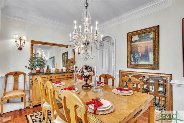 dining space with arched walkways, an inviting chandelier, ornamental molding, and light wood finished floors