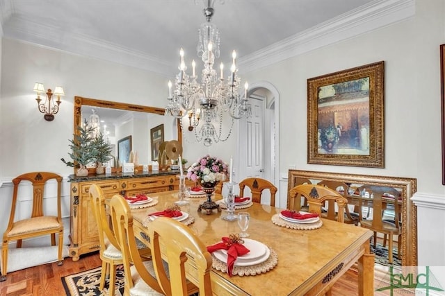 dining space featuring crown molding, arched walkways, light wood-type flooring, and a chandelier