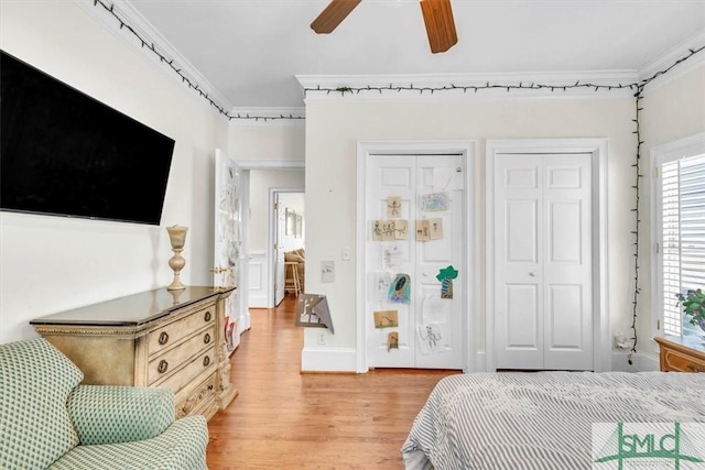 bedroom with light wood finished floors, two closets, a ceiling fan, and ornamental molding