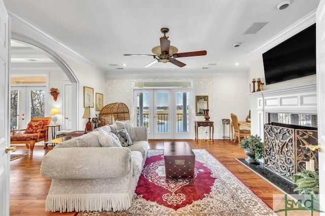 living room featuring a ceiling fan, ornamental molding, wood finished floors, french doors, and arched walkways