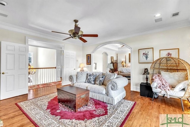 living room featuring arched walkways, a ceiling fan, ornamental molding, and light wood-type flooring