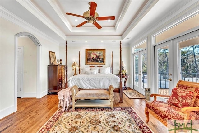 bedroom featuring light wood-style flooring, access to outside, arched walkways, crown molding, and a raised ceiling