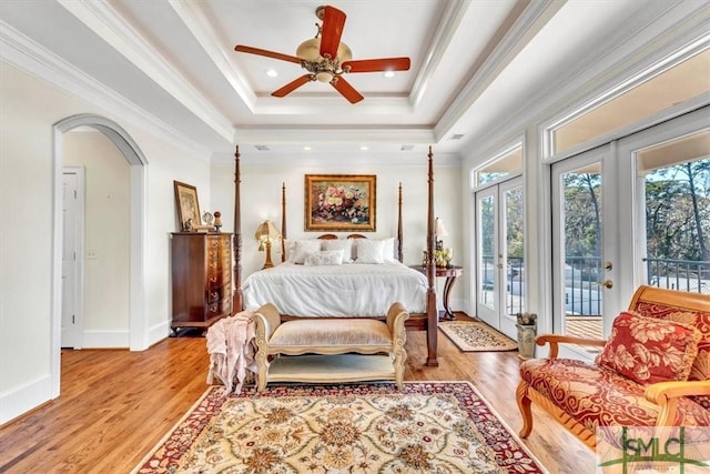 bedroom featuring a raised ceiling, arched walkways, access to exterior, and light wood finished floors