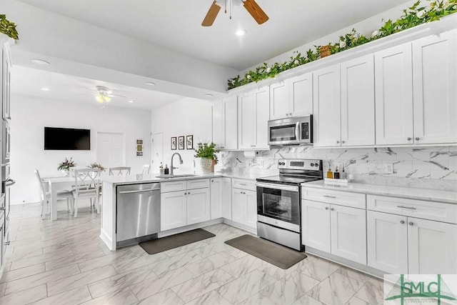 kitchen featuring a sink, backsplash, white cabinetry, stainless steel appliances, and a peninsula