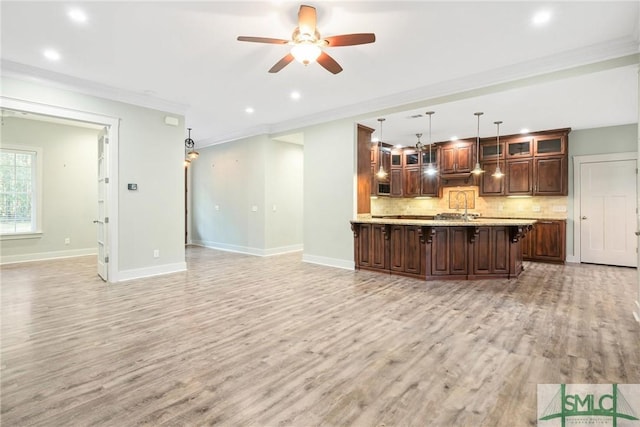 kitchen with light countertops, light wood-style floors, crown molding, open floor plan, and backsplash