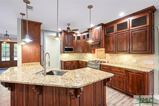 kitchen featuring a ceiling fan, a peninsula, a sink, stainless steel appliances, and backsplash