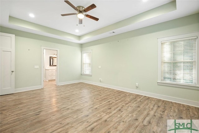 unfurnished room with visible vents, baseboards, light wood-type flooring, a tray ceiling, and a ceiling fan