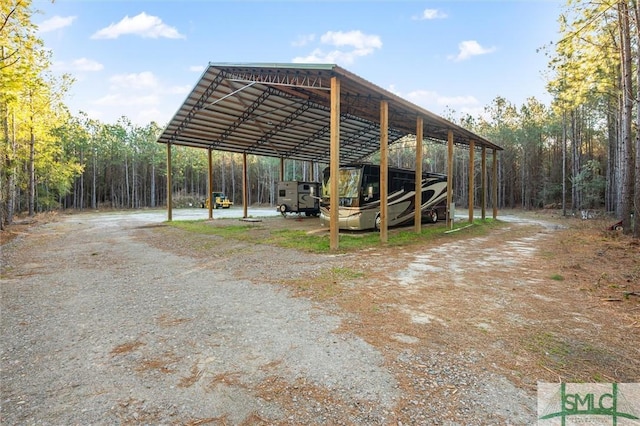 exterior space with a carport, a forest view, and dirt driveway