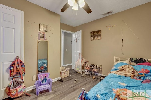 bedroom featuring visible vents, a ceiling fan, baseboards, and wood finished floors