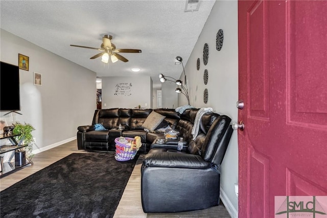 living room featuring a ceiling fan, baseboards, wood finished floors, visible vents, and a textured ceiling