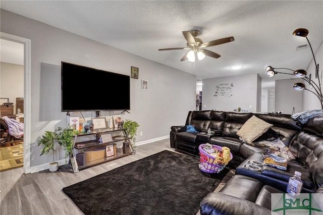 living room featuring wood finished floors, baseboards, visible vents, ceiling fan, and a textured ceiling