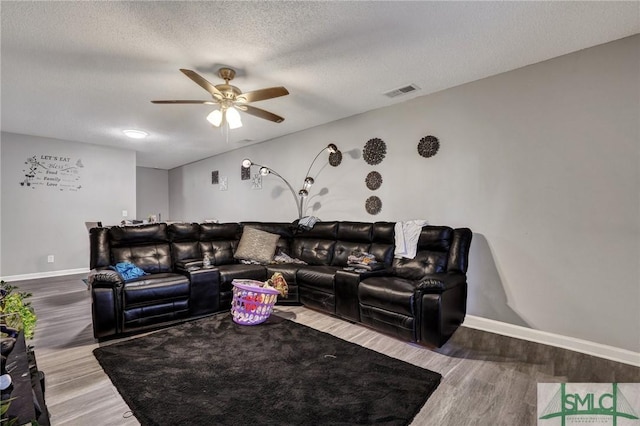 living area with visible vents, a ceiling fan, a textured ceiling, wood finished floors, and baseboards