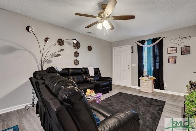 living room featuring visible vents, light wood-style flooring, a textured ceiling, and baseboards