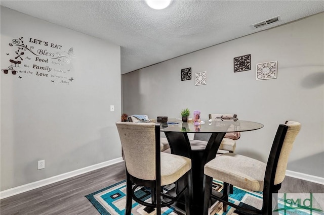 dining space featuring baseboards, wood finished floors, visible vents, and a textured ceiling